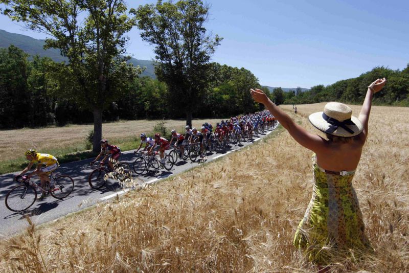 TF 0038 A woman in a wheat field cheers on a pack of riders as they cycle during the stage40 of the 